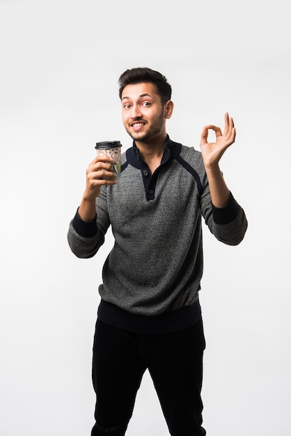 Jeune homme asiatique indien tenant une tasse de café en papier avec un capuchon en plastique noir isolé sur fond blanc dans le studio, café publicitaire