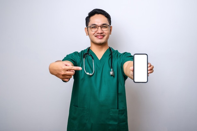 Jeune homme asiatique infirmière médecin portant des gommages et un stéthoscope à la recherche d'une caméra montrant un écran de smartphone vierge recommandant l'application