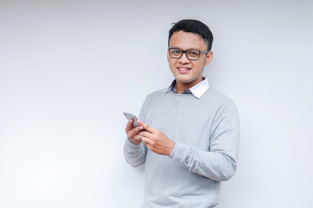 Un jeune homme asiatique intelligent est heureux et souriant lorsqu'il utilise un smartphone en arrière-plan de studio