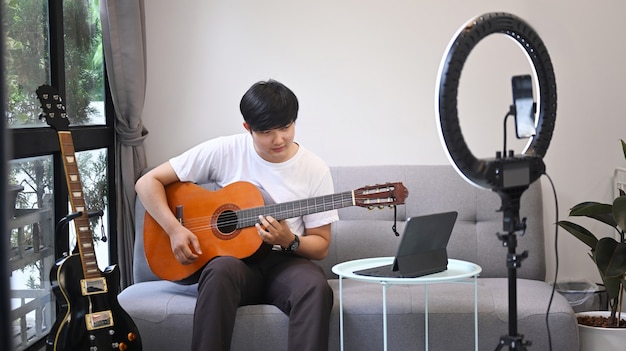 Jeune homme asiatique jouant de la guitare et diffusant un vlog en ligne à la maison.