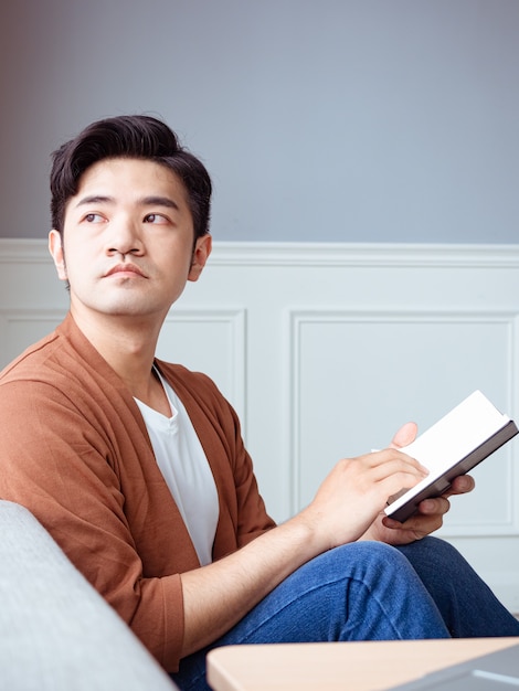 Jeune homme asiatique lisant un livre tout en se relaxant à la maison