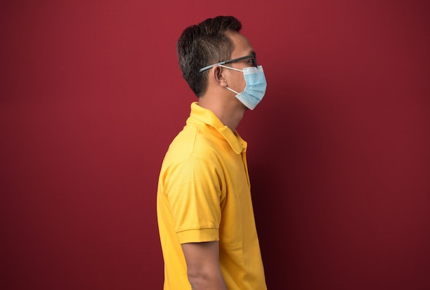 Jeune homme asiatique à lunettes portant un masque médical regardant sur le côté se détendre pose avec un visage naturel.