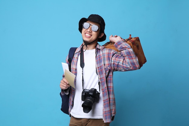 Photo jeune homme asiatique en lunettes avec un sourire positif voyage à l'étranger, tenant des billets et un sac