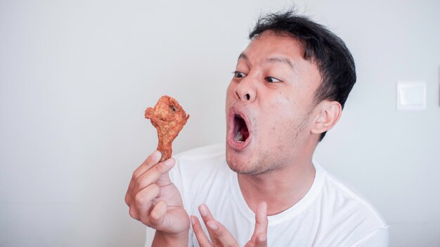 Un jeune homme asiatique mange du poulet frit, porte une chemise blanche, se sentant en colère et fou