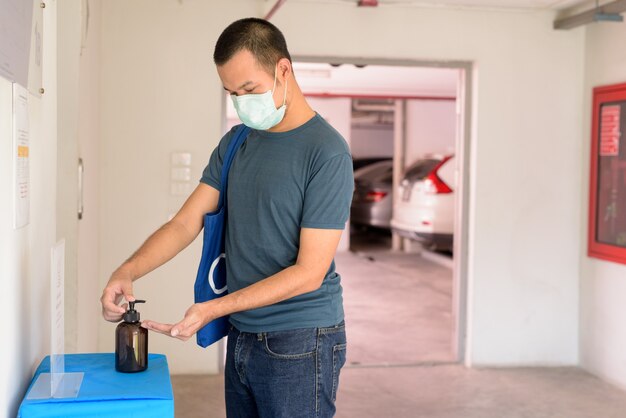 Jeune homme asiatique avec un masque utilisant un désinfectant pour les mains pour prévenir la propagation du coronavirus