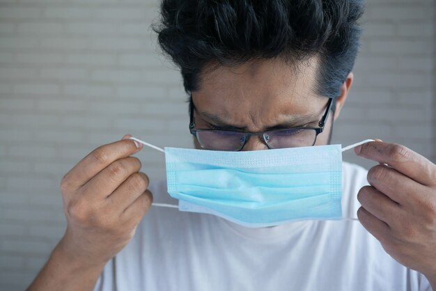 Jeune homme asiatique mettant un masque chirurgical à l'intérieur