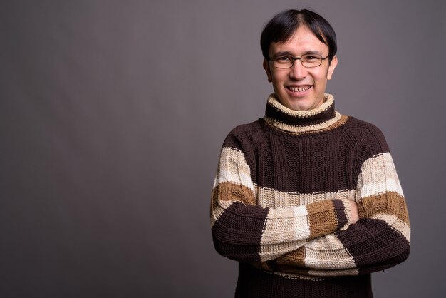 Jeune homme asiatique nerd portant un pull à col roulé contre un mur gris