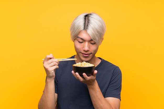 Jeune homme asiatique avec des nouilles au jaune isolé