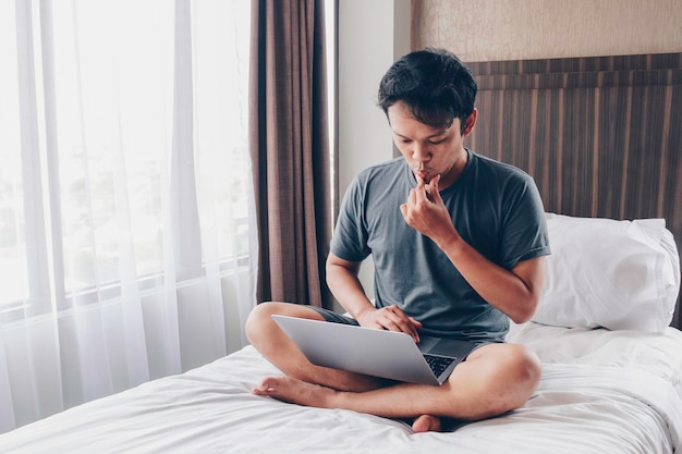 Jeune homme asiatique avec un ordinateur portable au lit est confus et stressé Concept de travail à domicile