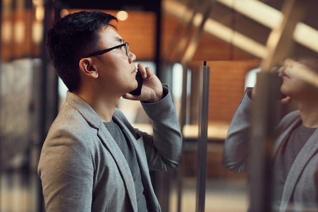 Jeune, homme asiatique, parler, par, smartphone, vue côté