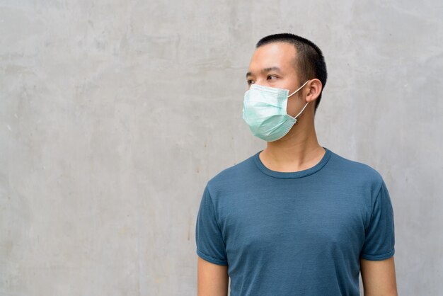 Jeune homme asiatique pensant avec un masque pour se protéger contre l'épidémie de coronavirus à l'extérieur