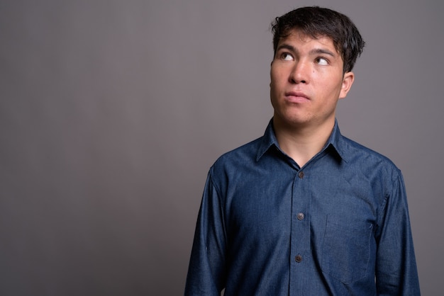 Jeune homme asiatique portant une chemise bleue contre le mur gris