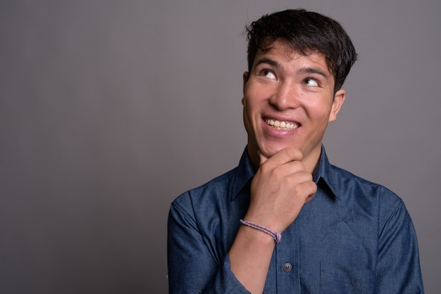 Jeune homme asiatique portant une chemise bleue contre le mur gris