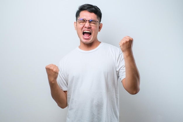 Jeune homme asiatique portant une chemise décontractée debout très heureux et excité faisant le geste du gagnant avec les bras levés souriant et criant pour le succès Concept de célébration