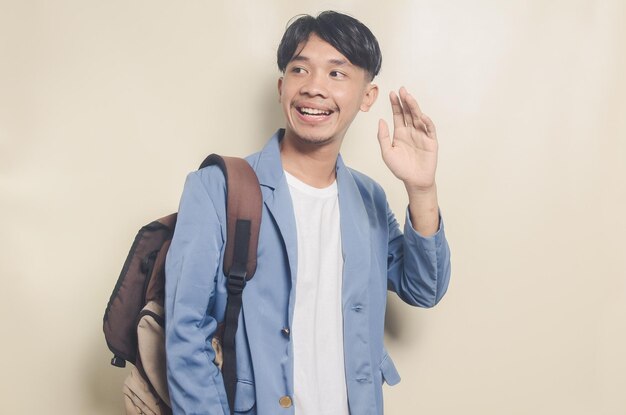 Jeune homme asiatique portant un costume d'université avec une expression saluant son ami tout en portant un sac