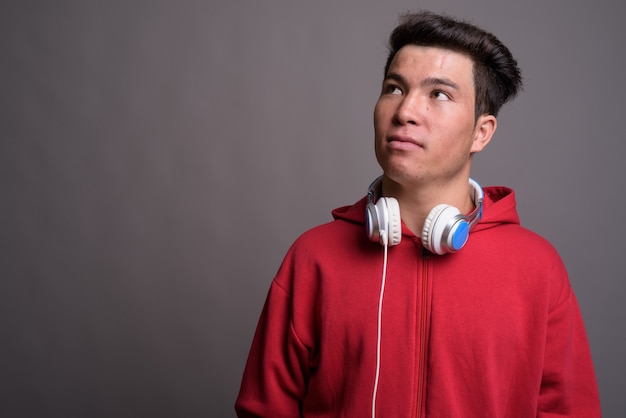 Jeune homme asiatique portant des écouteurs contre le mur gris