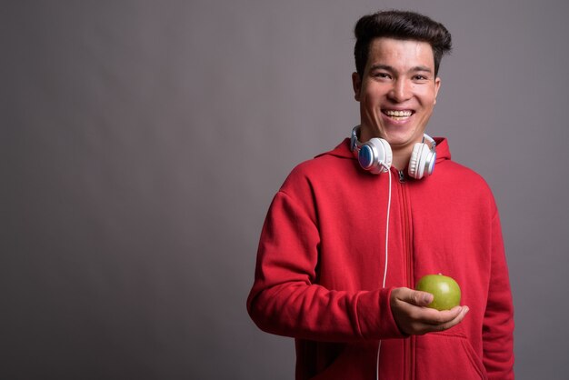 Jeune homme asiatique portant des écouteurs contre le mur gris