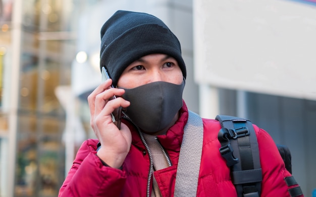 Jeune homme asiatique portant un masque de protection hygiénique sur son visage tout en prenant le téléphone, les soins de santé et la prévention des maladies par coronavirus, la grippe Covid19 dans un endroit bondé.