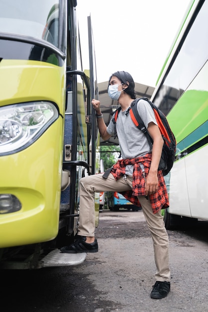 Jeune homme asiatique portant des masques faciaux montant dans le bus. Un homme portant un masque facial et portant un sac à dos monte dans le bus au terminal