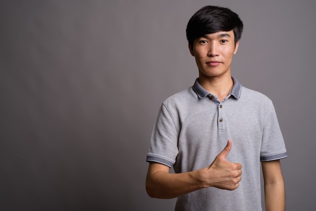 Jeune homme asiatique portant un polo gris contre un mur gris