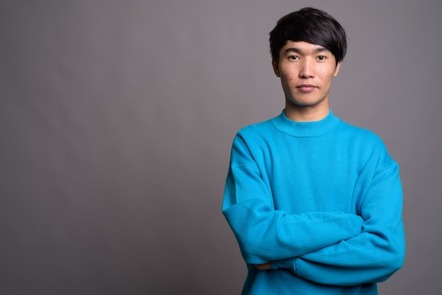 Jeune homme asiatique portant un pull bleu contre un mur gris