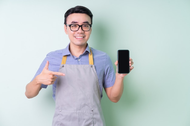 Jeune homme asiatique portant un tablier posant sur fond vert