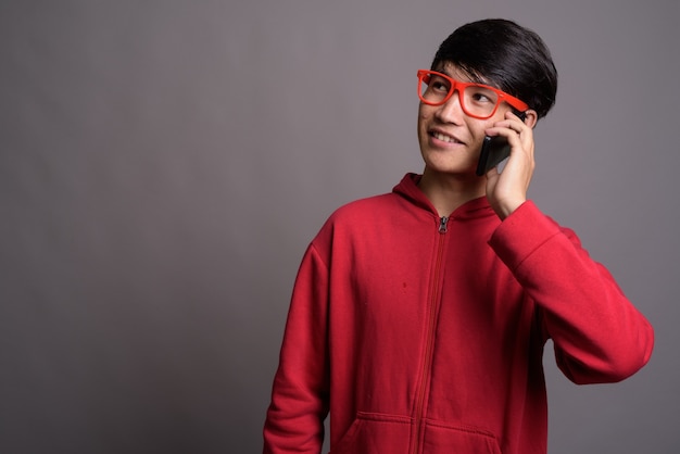 Jeune homme asiatique portant une veste rouge avec des lunettes contre gris