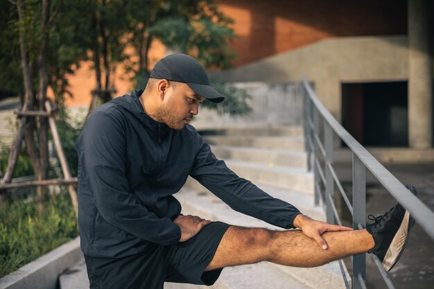 Jeune homme asiatique portant des vêtements de sport courant en plein air Portraits d'un homme indien qui s'étend de la jambe avant de courir sur la route