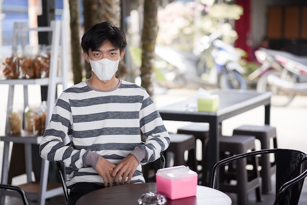 Un jeune homme asiatique porte un masque facial pour se protéger du virus, assis dans un café