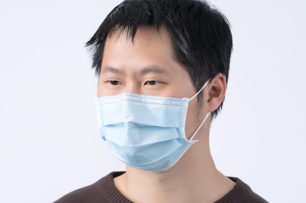 Jeune homme asiatique portrait se sentant malade portant un masque chirurgical bleu pour prévenir l'infection pollution de l'air isolé sur fond blanc découpé