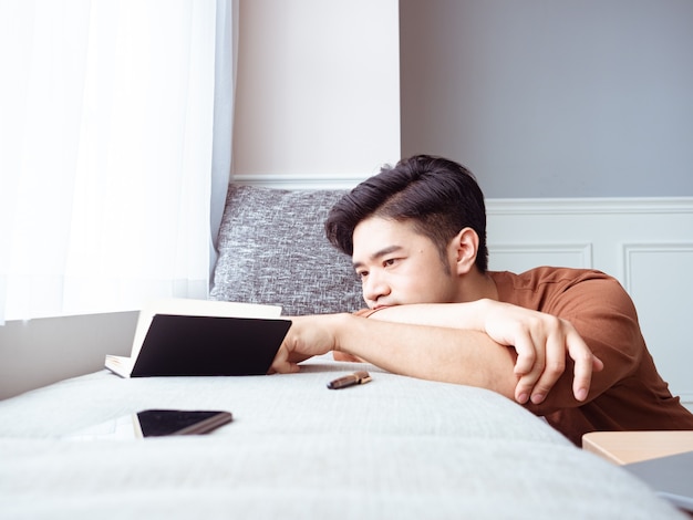 Jeune homme asiatique prenant une pause après avoir lu un livre à la maison