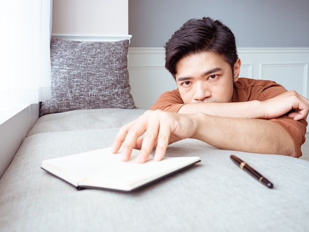 Jeune homme asiatique prenant une pause après avoir lu un livre à la maison