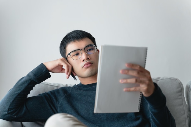 Jeune homme asiatique réfléchi dans des verres pensant et regardant notebookxA