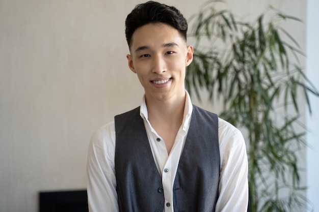 Jeune homme asiatique regarde à huis clos en souriant contre une plante luxuriante