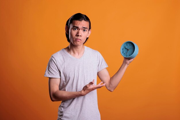 Jeune homme asiatique en retard, tenant une alarme rétro, ponctualité, calendrier des délais, concept de gestion du temps. Une personne a dormi trop longtemps le matin, un adolescent anxieux pointant vers une horloge vintage