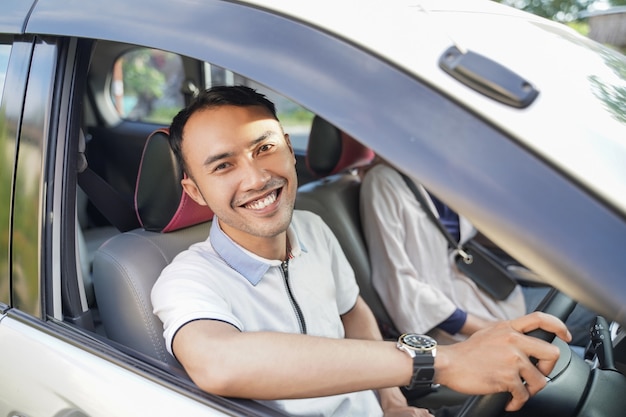 Un jeune homme asiatique riant en regardant la caméra en conduisant une voiture