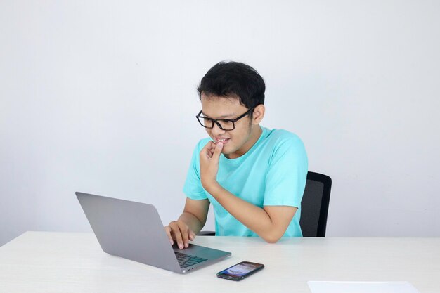 Jeune homme asiatique se sentant heureux et souriant quand il travaille sur un ordinateur portable sur la table Homme indonésien portant une chemise bleue