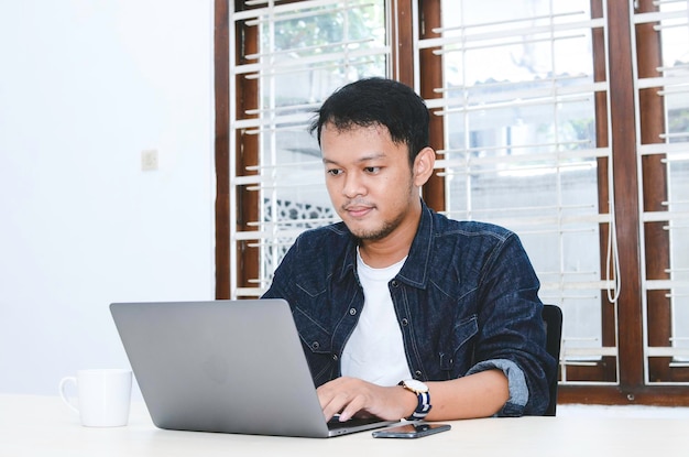 Jeune homme asiatique se sentant sérieux quand il travaille sur un ordinateur portable sur la table