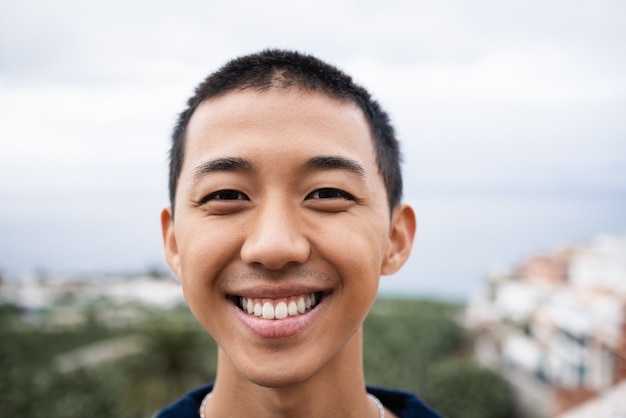 Jeune homme asiatique souriant à la caméra en plein air - Focus on face