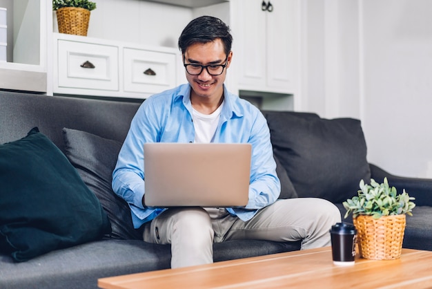 Jeune homme asiatique souriant se détendre à l'aide d'un ordinateur portable travaillant et réunion de vidéoconférence en ligne chat