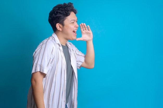 Jeune homme asiatique en style décontracté criant sur le côté annonçant une grande publicité sur un fond bleu
