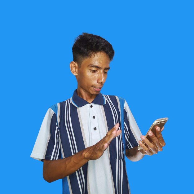 Jeune homme asiatique surpris en regardant un téléphone intelligent portant un t-shirt coloré sur un fond bleu isolé