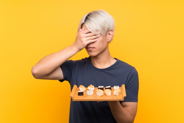 Jeune homme asiatique avec sushi couvrant les yeux par des mains