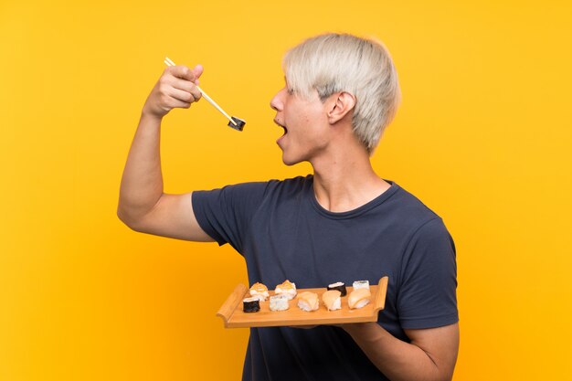 Jeune homme asiatique avec sushi sur jaune isolé