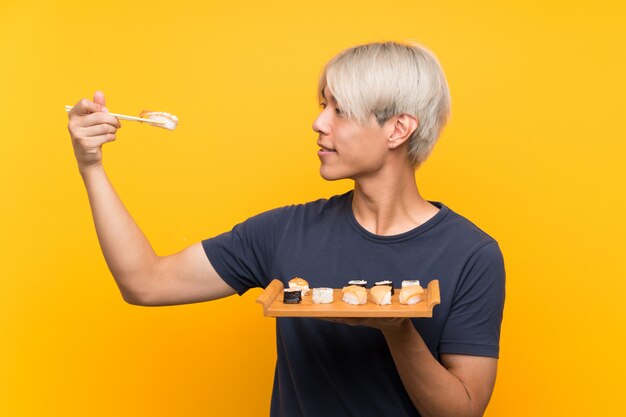 Jeune homme asiatique avec sushi sur jaune isolé