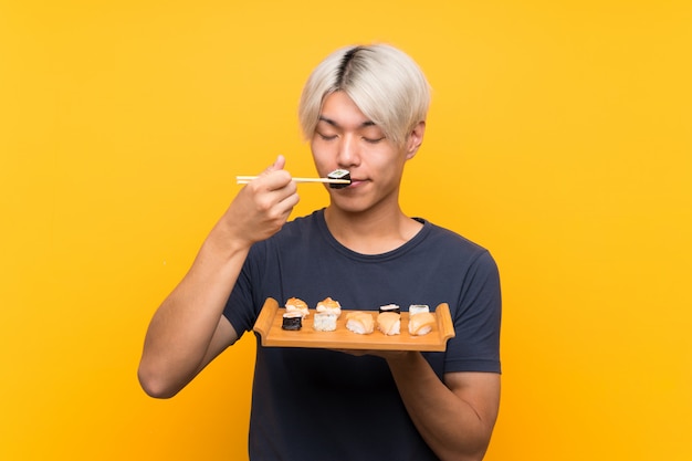 Jeune homme asiatique avec sushi sur jaune isolé