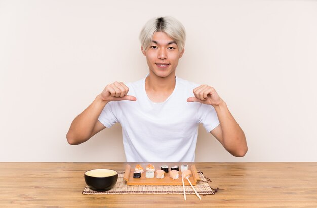 Jeune homme asiatique avec sushi à une table fier et satisfait