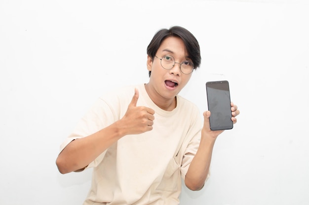 jeune homme asiatique en t-shirt beige tenant et montrant l'écran du téléphone avec un visage choqué euphorique heureux