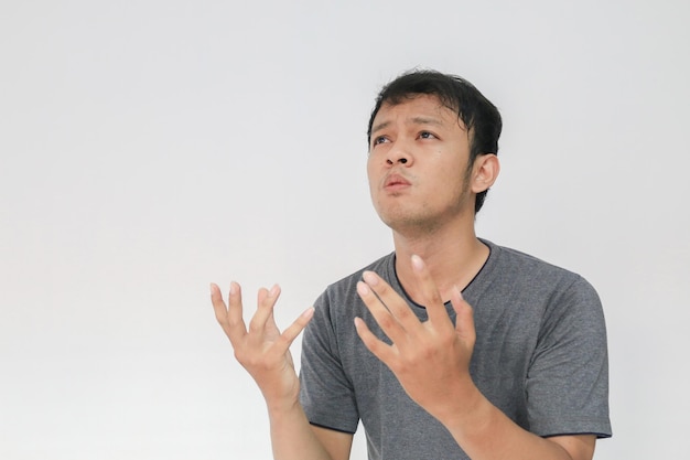 Jeune homme asiatique en t-shirt gris priant avec un visage triste