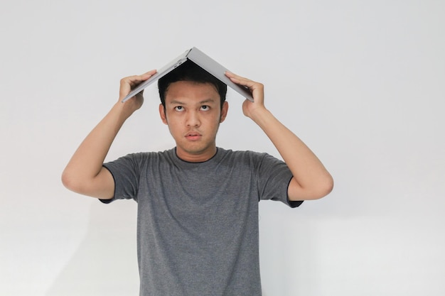 Jeune homme asiatique en t-shirt gris Se sentir stressé et confondre avec un ordinateur portable dans sa tête Jeune homme frustré et stressé au travail